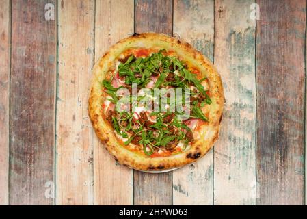 Pizza avec tranches de jambon cuit, fromage mozzarella, beaucoup de tomates déshydratées et feuilles de roquette Banque D'Images