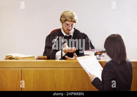 Présentez votre cas Un jeune juge sérieux assis dans la salle d'audience avec une expression faciale fougère. Banque D'Images