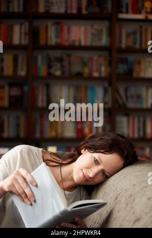 Dans son propre monde. Une jeune femme attirante se relaxant sur un canapé avec un espace livre - copie. Banque D'Images