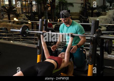 L'entraînement dirigé par un instructeur aide un beau client à effectuer des exercices dans un club de remise en forme, le concept de jouer du sport avec un loisir professionnel de gym Banque D'Images