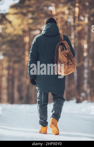 Un homme avec un sac à dos en tissu touristique, dans une forêt d'hiver, dans une veste et des bottes de trekking orange en plein air Banque D'Images