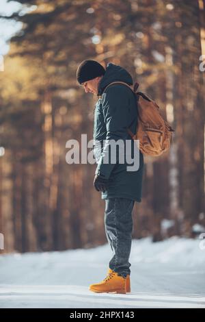 Un homme avec un sac à dos en tissu touristique, dans une forêt d'hiver, dans une veste et des bottes de trekking orange en plein air Banque D'Images