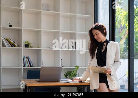 Femme asiatique attractive vérifiant les impôts, le solde de compte bancaire et le calcul des dépenses dans le salon à la maison Banque D'Images