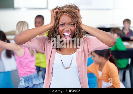 Je ne peux plus le prendre. Photo d'un jeune enseignant dans une salle de classe pleine d'enfants. Banque D'Images