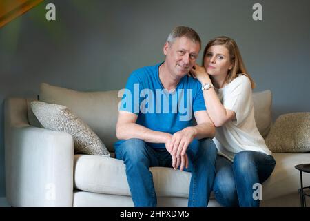 Un couple caucasien heureux rit tout en étant assis sur un canapé dans le salon. La femme déchoit son mari alors qu'elle est assise sur le canapé à la maison. Homme et femme passent du temps libre dans un appartement moderne dans le salon Banque D'Images