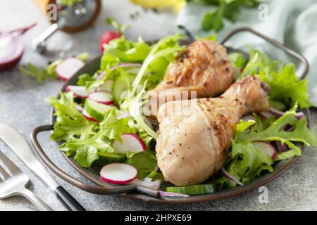 Saine alimentation propre. Viande et salade fraîche. Des pilons de poulet cuits et une salade végétalienne verte faite à partir d'un de feuilles vertes et de légumes de printemps sur un s. Banque D'Images