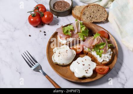 Petit-déjeuner ou brunch de Pâques. Délicieux petit déjeuner ou en-cas - œufs pochés et fromage à la crème pain de seigle complet, prosciutto, arugula sur un t de marbre Banque D'Images