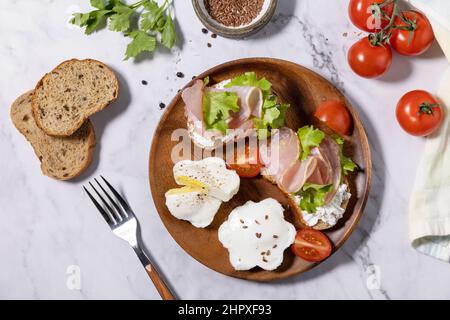 Petit-déjeuner ou brunch de Pâques. Délicieux petit déjeuner ou en-cas - œufs pochés et fromage à la crème pain de seigle complet, prosciutto, arugula sur un t de marbre Banque D'Images