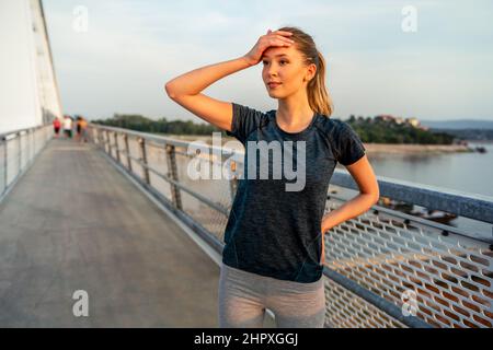 YYoung souriante femme en forme se reposant après un entraînement actif de fitness en plein air dans la ville Banque D'Images