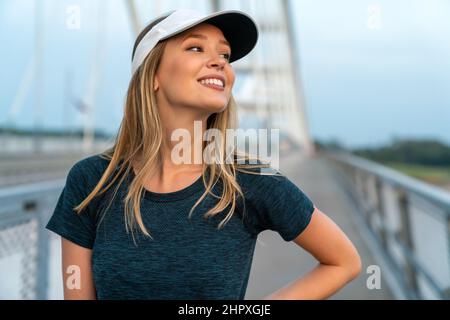 YYoung souriante femme en forme se reposant après un entraînement actif de fitness en plein air dans la ville Banque D'Images