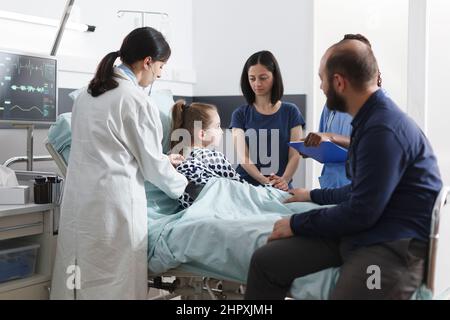 Pediatre vérifiant l'état de santé de malaise après l'intervention médicale alors que les parents mal soignants attendent les résultats de la consultation. Médecin généraliste consultant petite fille malade. Banque D'Images