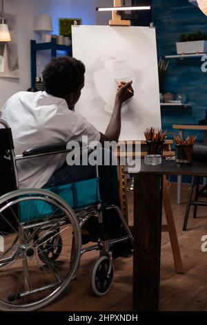 Jeune homme artiste en fauteuil roulant faisant de l'ombre à l'aide d'un crayon graphique travaillant à l'ilustration de vase pendant la leçon de peinture en studio d'art. Étudiant créatif avec un handicap esquissant une idée artistique Banque D'Images