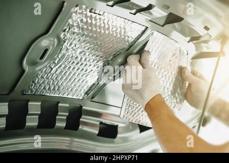 L'employé colle le matériau insonorisant à l'intérieur du capot de la voiture.Processus d'installation de l'isolation acoustique de la voiture. Banque D'Images