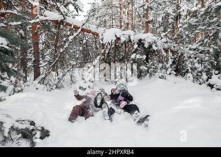 papa, maman et filles couché dans la neige dans la forêt d'hiver Banque D'Images