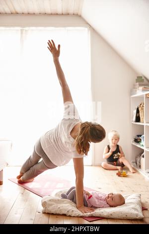 Ma mère aime bien le yoga. Prise de vue d'une jeune femme attrayante qui se joint à ses enfants tout en faisant du yoga. Banque D'Images