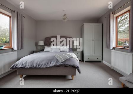 Chambre de luxe joliment meublée, décorée dans des tons de blanc, avec fenêtres à double aspect et tête de lit ornée de clous en tissu Banque D'Images