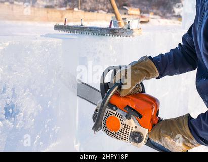 Le sculpteur coupe une forme d'un bloc de glace avec une scie à essence sur le lac Baikal. Banque D'Images