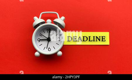 Réveil blanc avec texte Date limite sur le pense-bête. Sur fond rouge. Conceptuel Banque D'Images