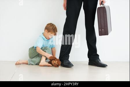 N'y allez pas Un jeune garçon tenant un teddyours et regardant triste parce que son père doit aller au travail. Banque D'Images