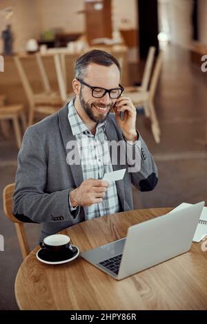 Homme joyeux utilisant un ordinateur portable et parlant sur le téléphone portable dans le café Banque D'Images