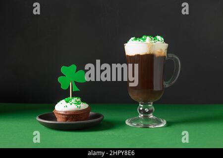 Café irlandais dans une tasse en verre et cupcake pour la Saint Patrick sur fond vert et noir. Bonne Saint Patrick. Banque D'Images