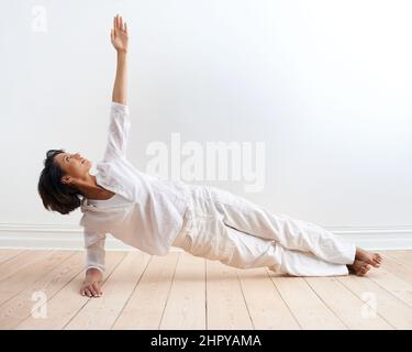Au sommet de sa santé et de sa forme physique. Une jeune femme en forme qui exécute la posture de planche latérale pendant sa routine de yoga. Banque D'Images