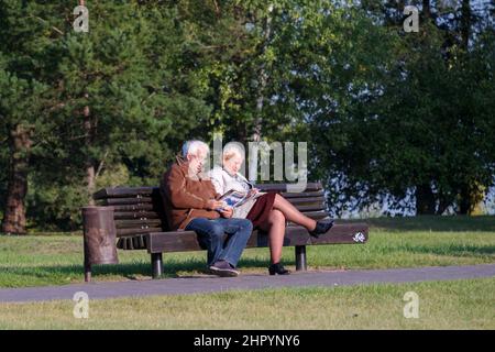 Aînés, couple de personnes âgées dans le parc sur un banc de lecture de magazines et de résoudre un mot croisé puzzle Banque D'Images