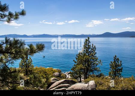 Vue sur les rochers lisses sur les rives du lac Tahoe et belle vue sur l'eau avec kayak ramer et montagnes au loin Banque D'Images