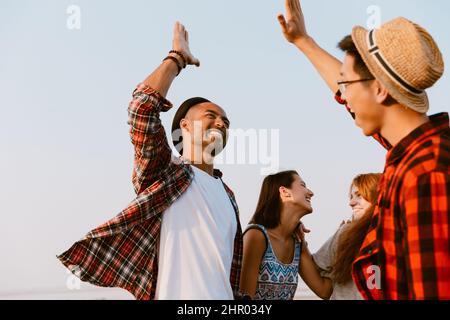 De jeunes amis multiraciaux s'amusent tout en donnant des cinq hauts en plein air Banque D'Images