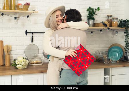 charmant coupé caucasien enfermé dans la cuisine, brunet homme donne à sa chère petite amie un cadeau inattendu dans un sac rouge. Photo de haute qualité Banque D'Images