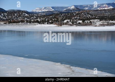 Grand format panoramique paysage d'hiver de neige a couvert la nature sauvage à travers un lac aux falaises rouges sur les montagnes au loin. Tourné dans l'Utah, aux États-Unis. Banque D'Images