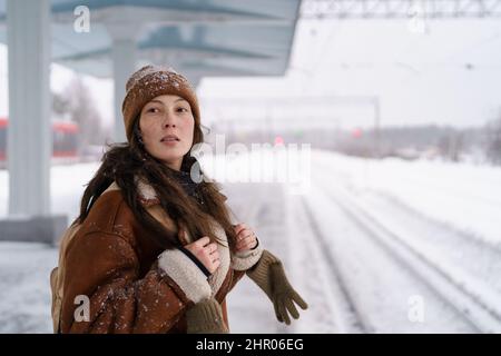 Femme attentionnée avec sac à dos debout sur une plate-forme enneigée et regardant le train d'arrivée Banque D'Images