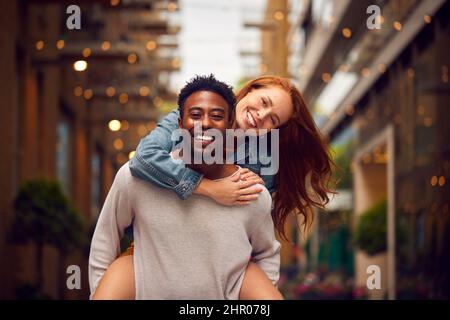 Portrait d'un jeune couple profitant de la vie urbaine se dirigeant pour la nuit avec l'homme donnant la femme Piggyback Banque D'Images
