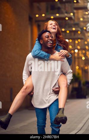 Portrait d'un jeune couple profitant de la vie urbaine se dirigeant pour la nuit avec l'homme donnant la femme Piggyback Banque D'Images