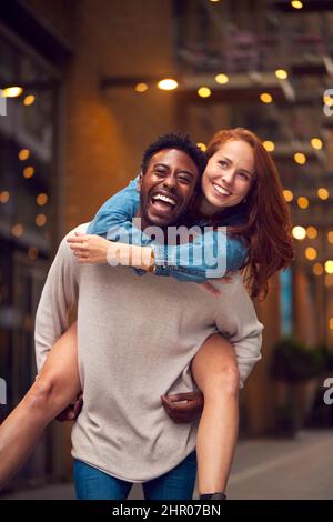 Portrait d'un jeune couple profitant de la vie urbaine se dirigeant pour la nuit avec l'homme donnant la femme Piggyback Banque D'Images