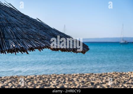 Parasol en paille de près, flou plage de sable vide. Journée ensoleillée en mer. Ciel bleu et mer, vacances d'été en Grèce Banque D'Images