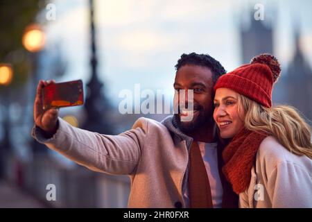 Couple dans la ville de Londres en plein air portant des Coats et des Scarves posant pour Selfie au téléphone en automne Banque D'Images