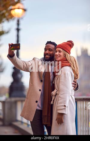 Couple dans la ville de Londres en plein air portant des Coats et des Scarves posant pour Selfie au téléphone en automne Banque D'Images