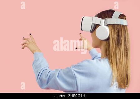 Fille dans un casque innovant jouant à des jeux vidéo, faisant l'expérience de VR, touchant des objets virtuels Banque D'Images