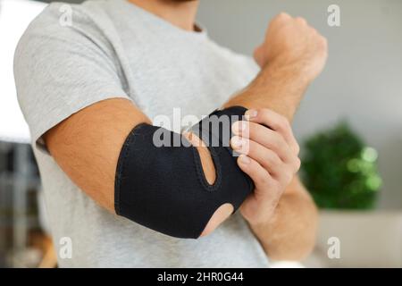 Bandage médical de soutien élastique noir sur le coude de l'homme qui se récupère de la blessure. Banque D'Images