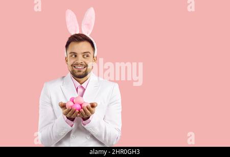 Homme heureux dans les oreilles de lapin tenant des oeufs de Pâques et regardant l'espace de copie sur le côté droit Banque D'Images