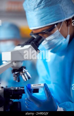 Gros plan sur une femme de laboratoire portant un EPI pour la recherche d'un vaccin avec le microscope Banque D'Images