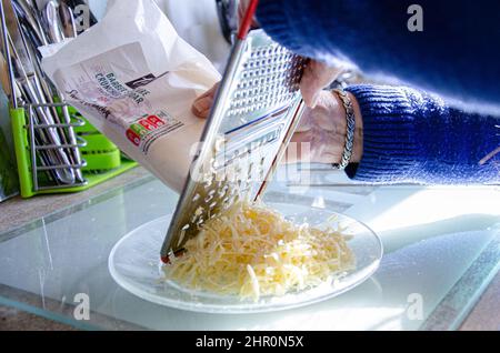 Vue rapprochée d'une femme qui râle du cheddar sur une assiette Banque D'Images