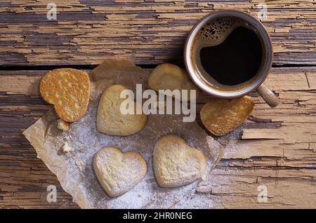 Vue en hauteur du café et des biscuits sablés en forme de cœur parsemés de sucre en poudre sur du papier sur fond de bois ancien Banque D'Images