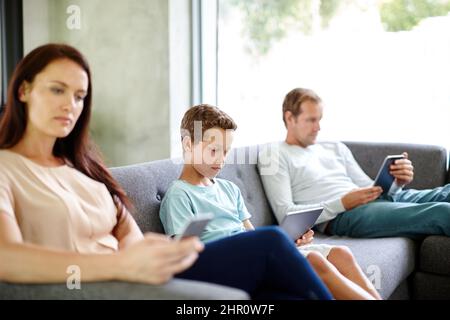 Laissé à eux-mêmes Prise de vue d'une famille de trois personnes assis séparément sur un canapé avec leurs propres appareils numériques. Banque D'Images