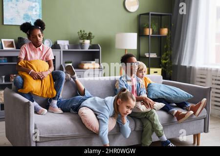 Divers groupes d'enfants regardent la télévision à la maison tout en se prélassant sur le canapé Banque D'Images