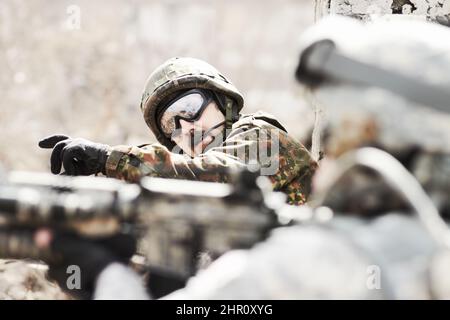 À la tête de son peloton. Profil d'un commandant donnant des ordres à ses soldats tout en étant allongé à plat sur le sol avec des armes à feu en main. Banque D'Images