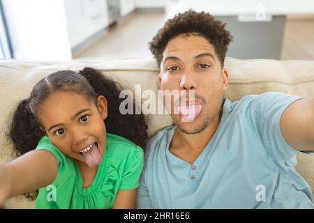 Un père et une fille biraciaux joueurs prenant le selfie tout en collant la langue à la maison Banque D'Images