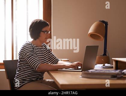 Administrateur du matin Photo courte d'une femme assise à un bureau chez elle et travaillant sur un ordinateur portable. Banque D'Images