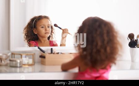 Je vais ressembler à ma maman. Photo d'une petite fille appliquant un fard à joues dans le miroir. Banque D'Images